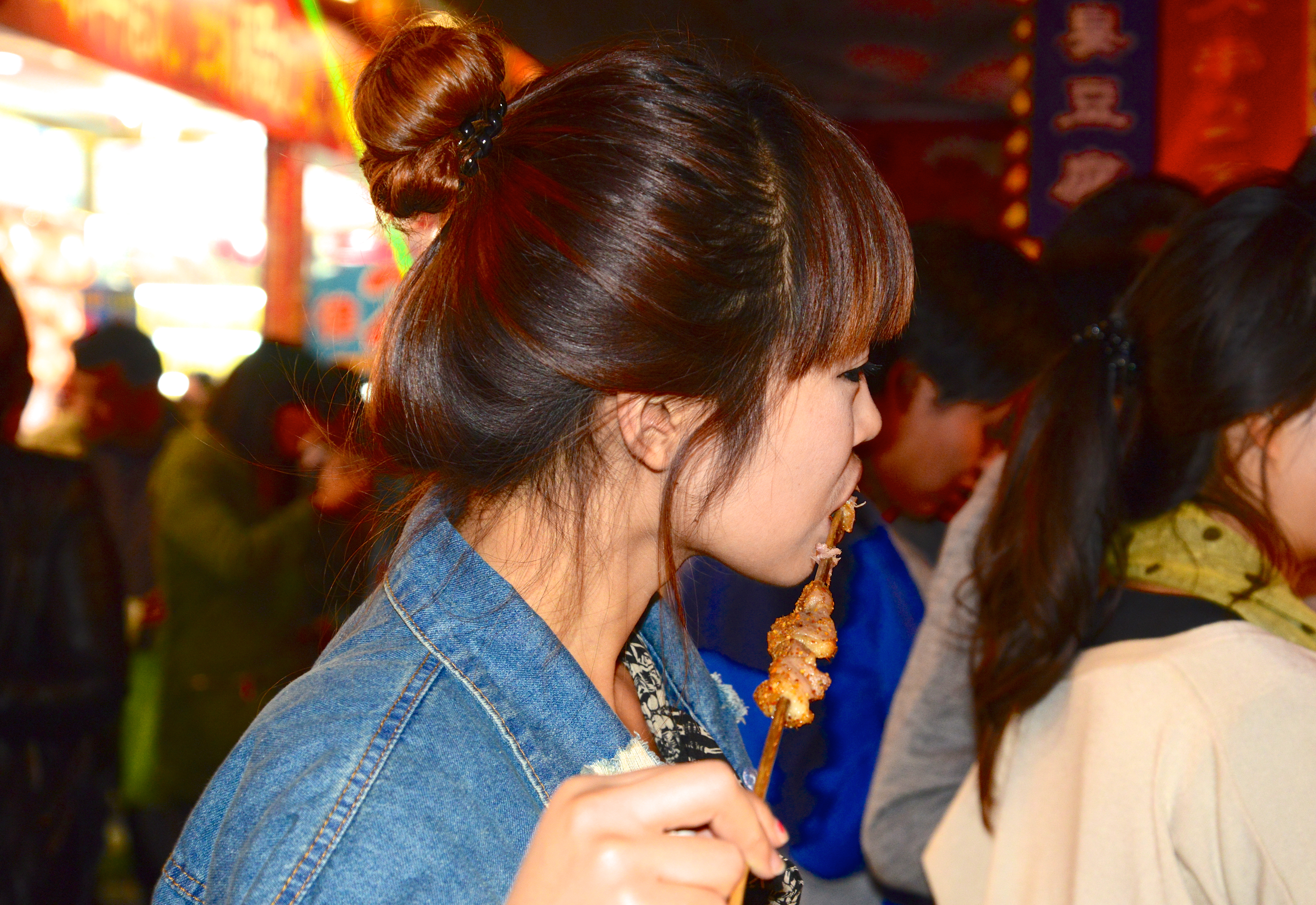Garota chinesa comendo petiscos na Rua das Comidas Exóticas.